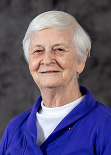A woman with short white hair wearing a white shirt under a bright blue jacket