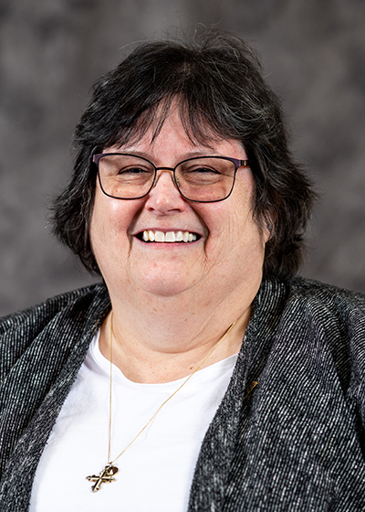 woman with short dark hair with glasses wearing a white shirt and gray cardigan sweater