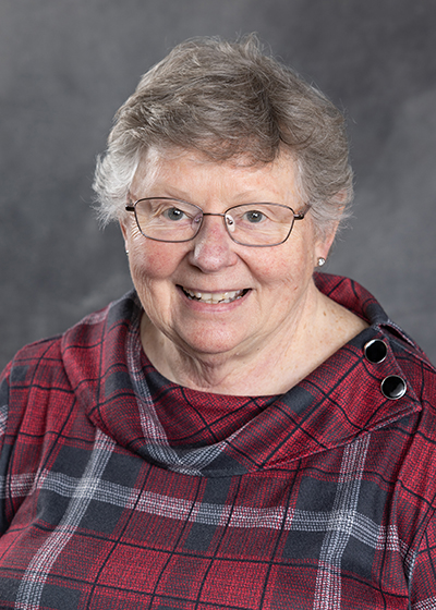 woman with short gray hair wearing glasses and wearing a red, black and gray plaid blouse
