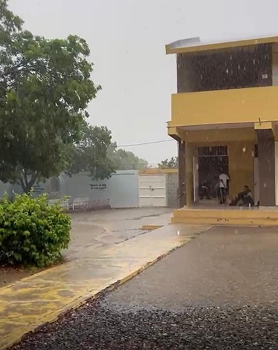 Rain collects in large puddles on an enclosed schoolyard with a sidewalk and a bush